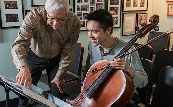A student holding a cello and a professor looking at sheet music