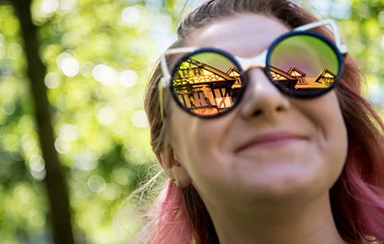 A smiling student, with the reflection of the Humanities Building in her sunglasses