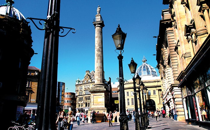 People walking past lampposts on the stone walkways of Newcastle, England