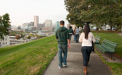 A group of students walking down a sidewalk on a hill with the Baltimore skyline in the background