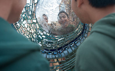 A pair of people looking at their reflection on a piece of art created from a mosaic of glass